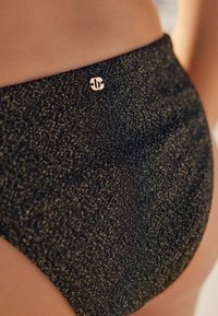 Aukšto liemens juodos bikini kelnaitės su tekstūruotu blizgiu paviršiumi. Savybė - mažas auksinis logotipas ant juosmens.