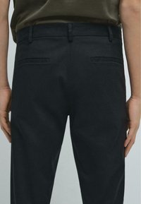 Černé kalhoty z tkané látky, se standardním střihem, dvěma zadními kapsami a hladkým povrchem. Pas je plochý.