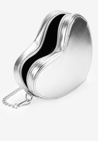 Bolso plateado en forma de corazón con doble cremallera, textura metálica suave, interior negro y una correa de cadena para llevarlo.