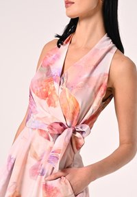 Robe portefeuille florale en tissu rose clair avec des motifs abstraits aux couleurs pastel. Présente un décolleté en V profond et une ceinture à nouer à la taille.