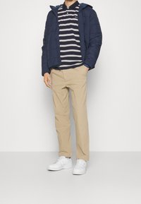 Doudoune marine à capuche, polo rayé marine et blanc, chinos beige, et baskets blanches. Tissu lisse, coupe décontractée.