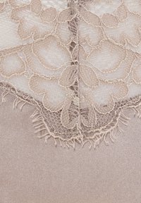 Spitzenrand in sanftem Beige mit floralen Mustern und fransigen Kanten, der auf glattem Satin in passendem Farbton liegt.