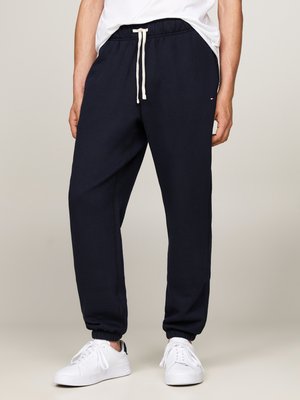 Marineblå joggebukser med elastiske mansjetter og snøring i livet; laget av et mykt materiale, med en liten logodetalj på siden.