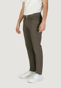 Pantaloni marroni slim-fit in misto cotone con tasche frontali e una texture liscia, abbinati a sneaker bianche.