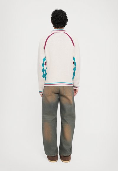 Pull en tricot, crème avec des motifs en losange turquoise et bordeaux, présentant un col et des poignets côtelés. Associé à un jean large bleu clair délavé.