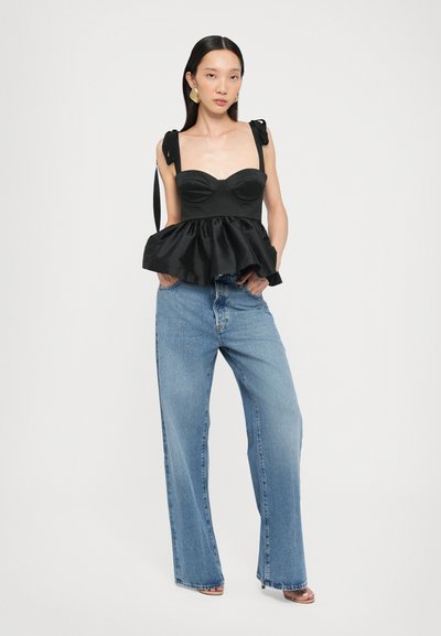 Black peplum top with wide straps and a fitted bodice, paired with high-waisted light blue wide-leg jeans. Smooth texture, casual design.