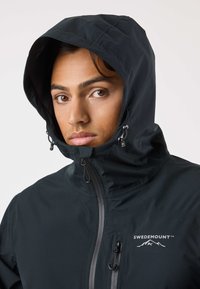 Black waterproof jacket with a hood, featuring a full zipper and a logo on the left chest. Textured fabric and adjustable drawstring details.