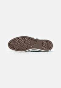 Suela de zapato de goma marrón con patrón texturizado de agarre y acento blanco a lo largo del borde, con logotipo de la marca y elementos de diseño simétricos.