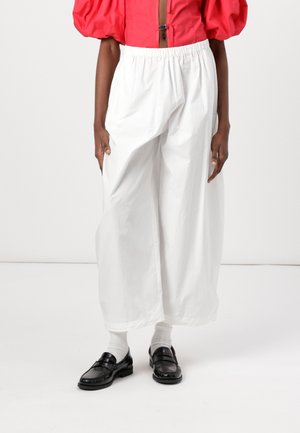 Pantaloni bianchi a gamba larga con una vita elasticizzata, realizzati in tessuto leggero. Abbinati a mocassini neri e calzini bianchi.