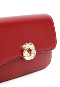 Borsa a tracolla in pelle rossa con chiusura a pattina, dotata di una fibbia a forma di nodo dorato e cuciture tonali lungo i bordi. Texture liscia.