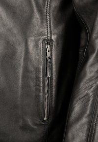 Schwarze Lederjacke mit einer Nahaufnahme des silbernen Reißverschlusses, die die glatte Textur und die detaillierte Naht an der Seite zeigt.