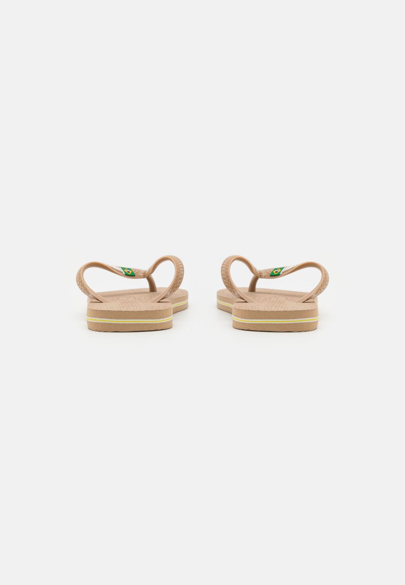 Tongs en caoutchouc marron avec des semelles texturées, deux brides courbées et un petit logo vert et jaune près du talon. Semelle de couleur claire avec une rayure.