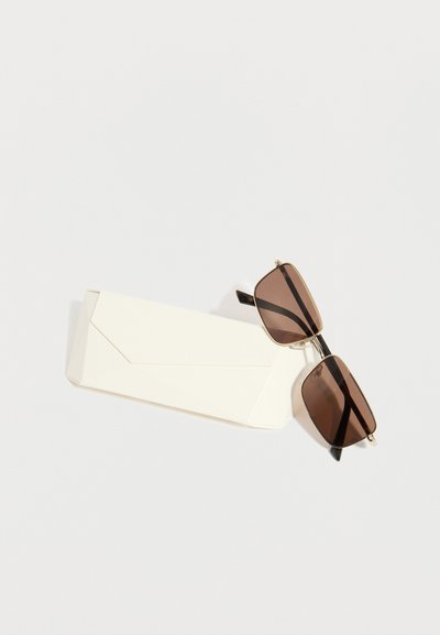 Ορθογώνια γυαλιά ηλίου με καφέ φακούς και λεπτά χρυσά πλαίσια, τοποθετημένα σε λευκή διπλωμένη θήκη γυαλιών ηλίου σε απλό φόντο.