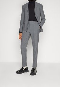 Szary garnitur o slim fit, noszony na czarnym golfie. Całość uzupełniają błyszczące czarne mokasyny i czarne skarpetki.