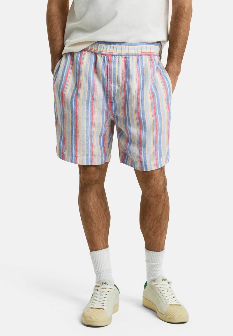 Gestreifte Shorts aus leichtem Material mit blauen, roten und gelben Linien; elastischer Bund; seitliche Taschen; kombiniert mit weißen Sneakern und Socken.