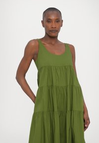 Abito verde senza maniche con un design a più strati. Realizzato in tessuto morbido, presenta un collo rotondo e sezioni arricciate per un volume aggiuntivo.