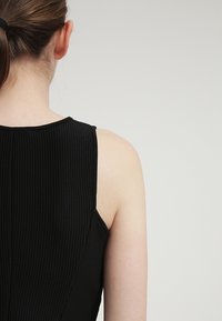 Top sin mangas negro con textura acanalada y escote suavemente curvado, mostrando la espalda y los hombros, con un tejido suave y elástico.