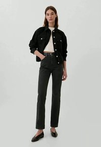 Casaco de ganga preto com fecho de botão, blusa branca justa, calças pretas de cintura alta e sapatos planos escuros. Design simples e moderno.
