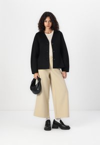 Svart cardigan med knapper, beige vide bukser og svarte kraftige loafers. Tilbehøret inkluderer en svart håndveske. Strikket topp under.