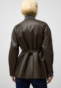 Giubbotto in pelle marrone con vita regolabile, caratterizzato da una vestibilità comoda e una finitura testurizzata, abbinato a un colletto grigio e maniche lunghe.