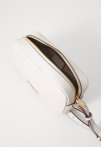 Borsa a tracolla bianca in pelle con finitura testurizzata, cerniera dorata e tracolla regolabile. L'interno presenta una fodera marrone con motivo.