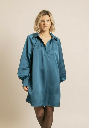 Robe en satin teal avec un col, de longues manches bouffantes et un décolleté en V. Texture lisse et coupe décontractée, se terminant au-dessus du genou.