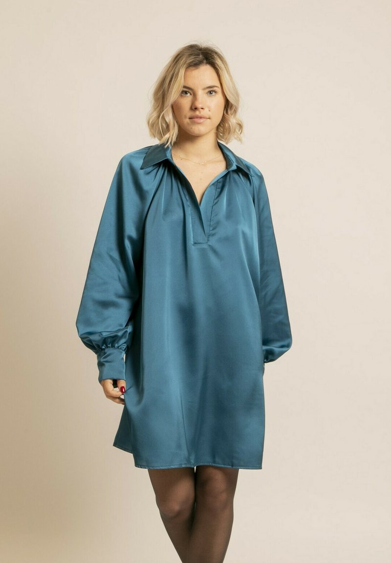 Robe en satin teal avec un col, de longues manches bouffantes et un décolleté en V. Texture lisse et coupe décontractée, se terminant au-dessus du genou.