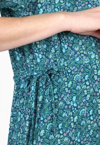 Blumengemusterteres Kleid aus türkisfarbener Stoff mit Blau-, Pink- und Grüntönen. Die Taille hat ein Stoffband zur Anpassung.