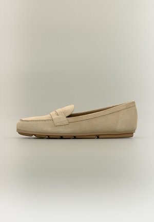 Beige semsket dameslipper med en lav gummisåle delt i segmenter og detaljert med en sydd rem på en nøytral bakgrunn.