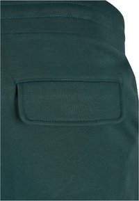 Gros plan sur un tissu vert foncé avec une poche à rabat rectangulaire présentant des coutures visibles le long des bords.