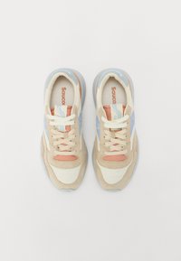 Beige og lyseblå sneakers med mokka og nettingmaterialer, som har en fremtredende logo, snørebånddesign og teksturert gummisåle.
