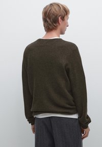 Mørkeolivengrøn strikket sweater med afslappet pasform, sænkede skuldre og ribstrik, parret med grå lærredsbukser med smalle striber.
