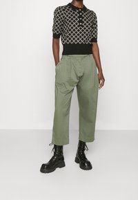 Czarna dzianinowa koszulka polo z geometrycznym wzorem, w zestawieniu z luźnymi oliwkowymi spodniami i czarnymi sznurowanymi bojówkami.