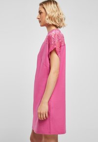 Roze katoenen jurk met korte mouwen, voorzien van kantaccenten op de schouders. Eenvoudige, ontspannen pasvorm en knielange ontwerp.