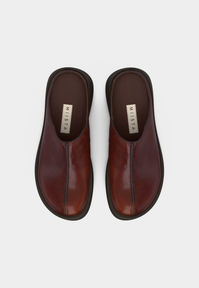 Ζευγάρι καφέ δερμάτινα καλοκαιρινά παπούτσια χωρίς κορδόνια με μαύρες σόλες και ορατές ραφές, σε θέα από πάνω πάνω σε λευκό φόντο.