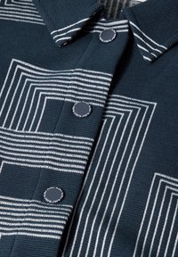 Šedobuněčná košile navy modré barvy s žebrovanou texturou, zdobená bílými geometrickými pruhy a kontrastními knoflíky. Má límeček a zapínání na knoflíky.