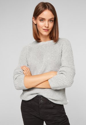 Hellgrauer Strickpullover mit rundem Halsausschnitt und Dreiviertelärmeln, der ein strukturiertes Muster und gerippte Akzente aufweist, kombiniert mit schwarzen Jeans.