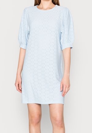 Woman wearing light blue perforated knee-length dress with puffed short sleeves and round neckline, standing against plain background.