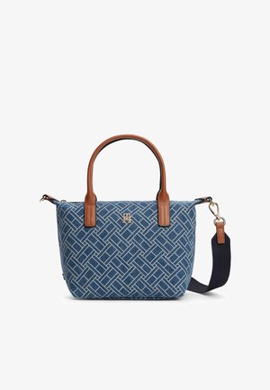 Jeanstasche mit braunen Ledergriffen, verziert mit einem geometrischen Muster, goldfarbenem Logo und verstellbarem marineblauem Schultergurt. Kompakte rechteckige Form.