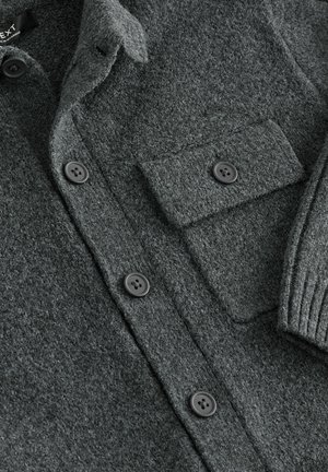 Mørkegrå strikket skjortejakke lavet af tekstureret stof med knaplukning foran, brystlomme og ribbede ærmekanter.