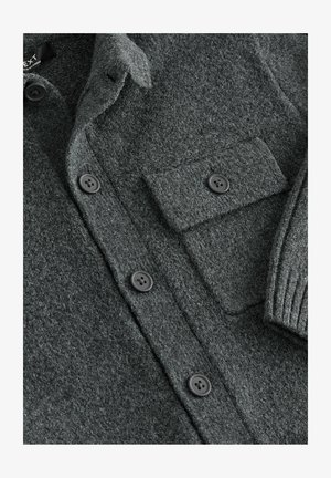 Tumši pelēka adīta krekla jaka no teksturētas auduma, ar pogām priekšpusē, krūšu kabatu un ribotām piedurkņu aprocēm.