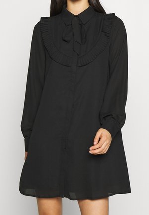 Sort kjole lavet af lette stoffer, med plisseret krave, knapper foran og lange ærmer med samlede manchetter. Enkel design.