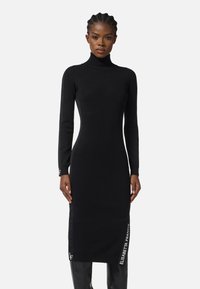 Robe noire à manches longues en col roulé au design ajusté, présentant une texture tricot lisse et des accents de marque blanche le long de l'ourlet.