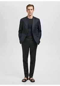 Een donkerblazer over een zwarte, getailleerde T-shirt, in combinatie met een nauwsluitende pantalon en zwarte sandalen. Gladde stof met een strak, minimalistisch ontwerp.