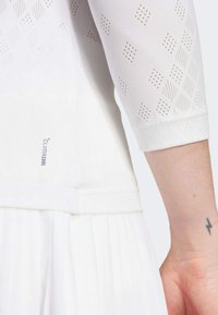 White dress with a textured pattern of small diamonds and dots. Features three-quarter sleeves and a pleated hem. Branded with "Climacool."