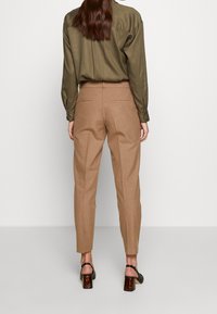 Brown tailored pants with a tapered leg and clean back pockets, paired with a green blouse and black high-heeled sandals.