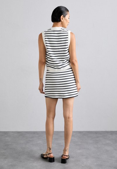Sømløs, tætsiddende tanktop og mini skirt sæt i hvid med navy striber. Har en blød tekstur og en ribbet talje. Sorte hælede sandaler.