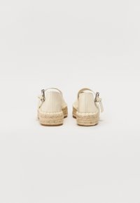 Espadrilles con parte superior de cuero beige, suela de yute trenzado y correa al tobillo. Presentan una textura suave y una forma redondeada.