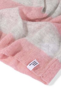 Manta suave y ligera de tejido en tonos rosa pastel y gris claro, con un acabado texturizado y una etiqueta en el borde inferior.