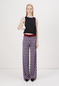 Zwarte crop top met een ronde halslijn, gecombineerd met wijdvallende broek met een geometrisch patroon in blauw, rood en wit en een bordeauxrood elastische tailleband.